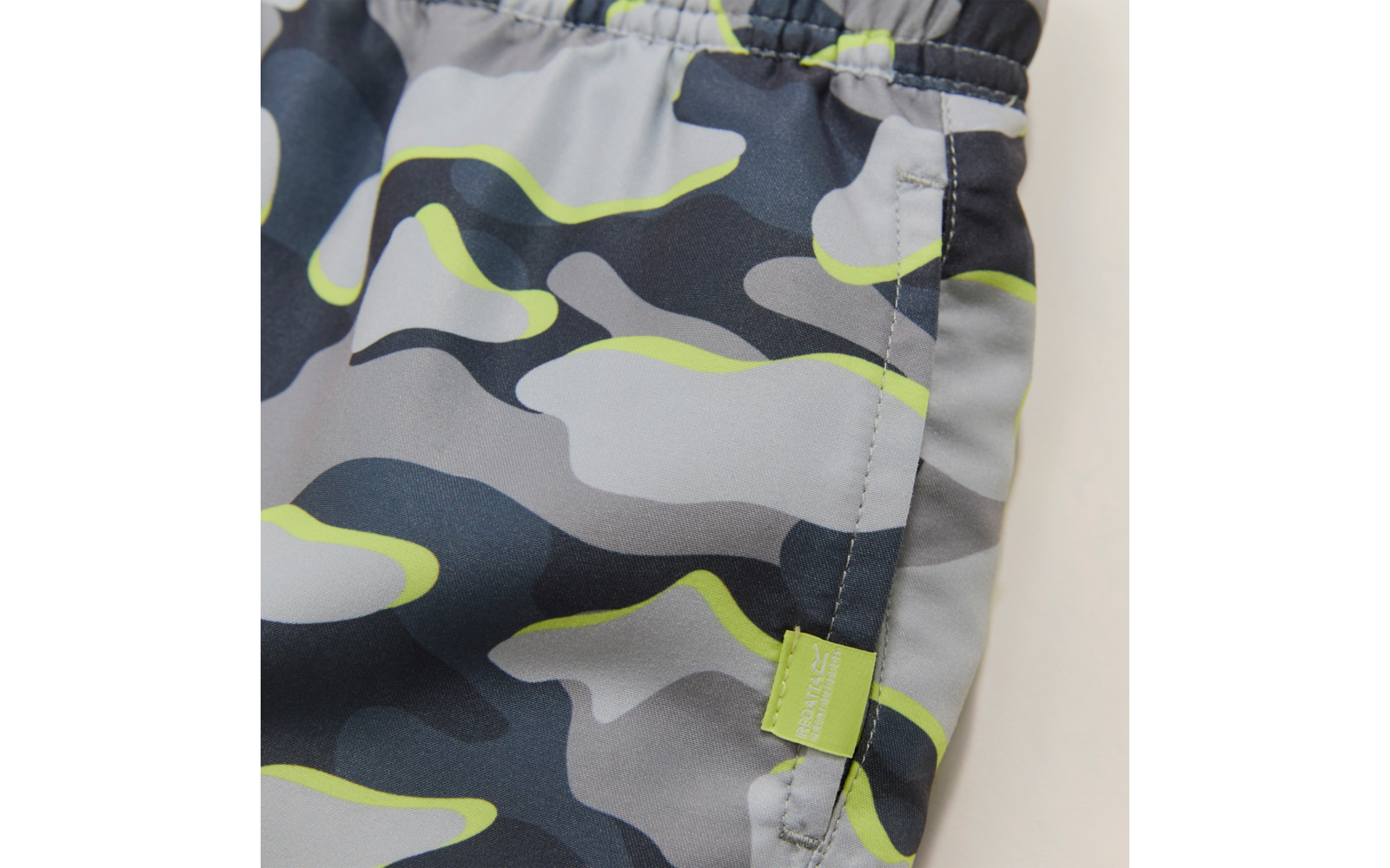 Nahaufnahme eines Kleidungsstücks mit elastischem Bund, Seitennähte, grauem und dunkelblauem Camouflage-Muster mit neongelben Akzenten, kleinem grünen Stoffetikett mit weißer Schrift