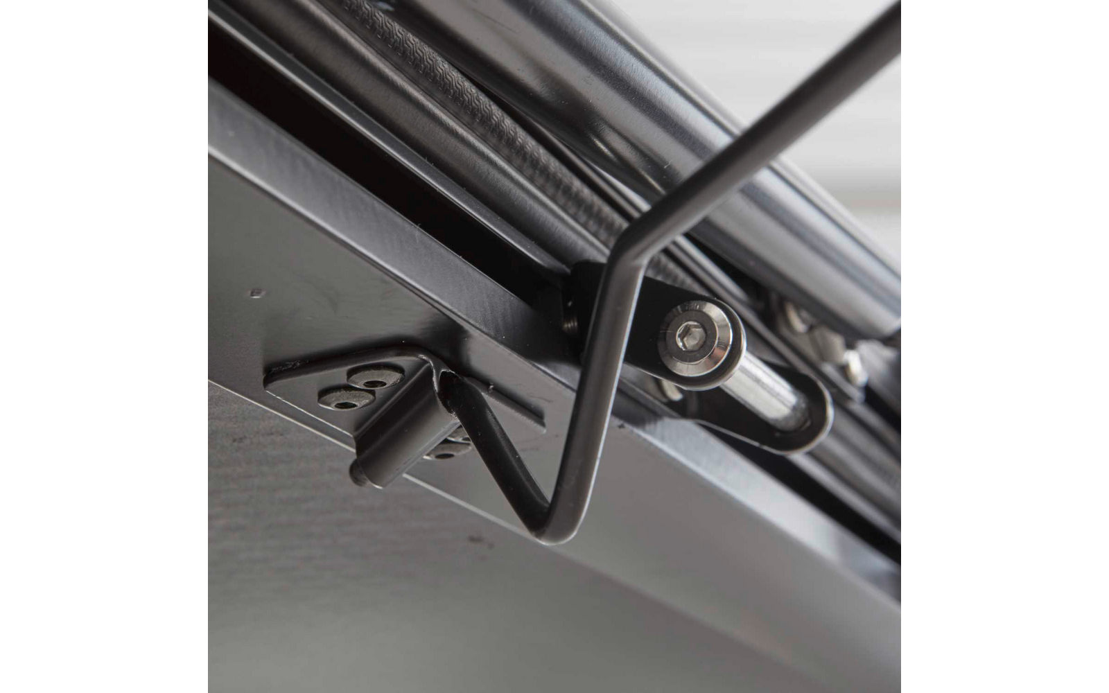 Nahaufnahme einer Metallstange mit Bolzen und schwarzem Metallbügel unter einer grauen, strukturierten Oberfläche