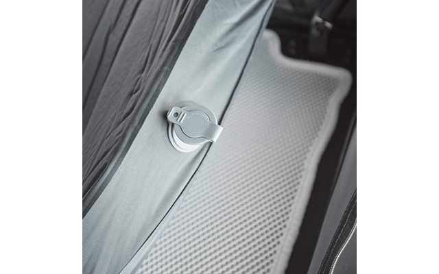 Nahaufnahme eines grauen Stoffteils mit runder weißer Kunststoffhalterung mit Clip, daneben eine hellgraue, genoppte Antirutschmatte und der Rand eines schwarzen Polstersitzes