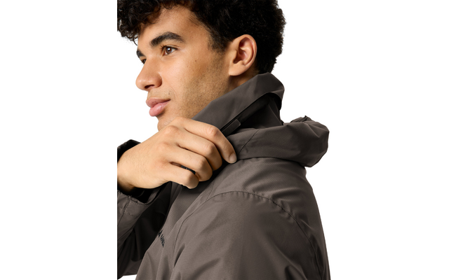 Person im Profil mit kurzen, dunklen, lockigen Haaren, die mit der Hand die Kapuze einer dunkelgrauen Jacke hochzieht