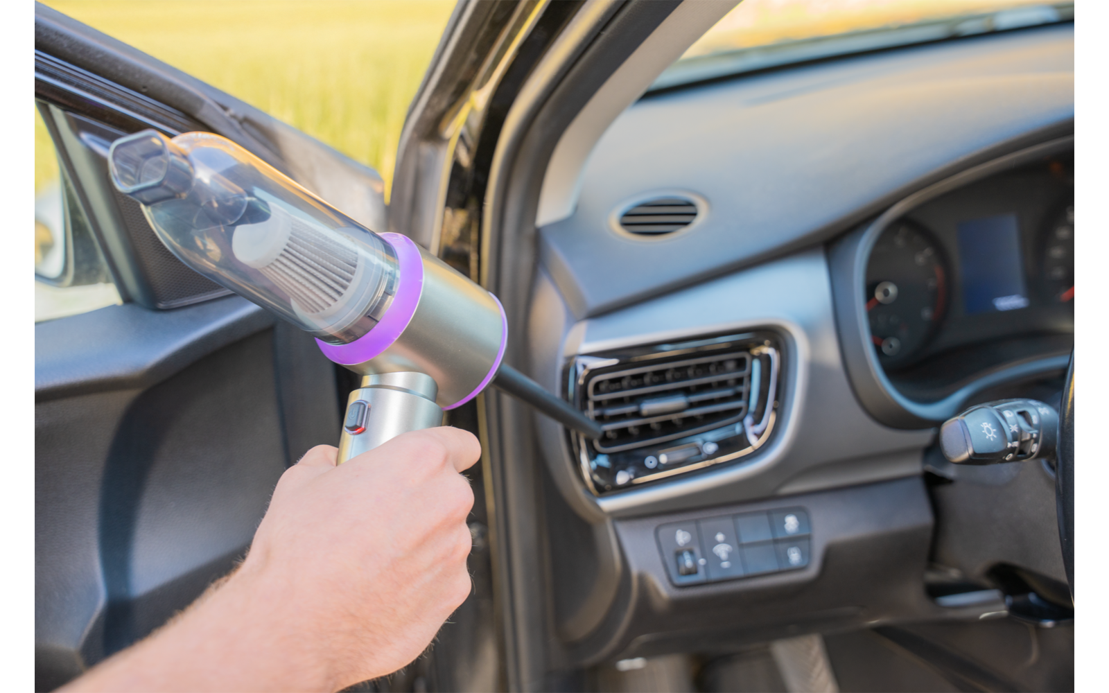 Main tenant un petit aspirateur portable près du panneau de porte et de la grille d'aération du tableau de bord d'une voiture