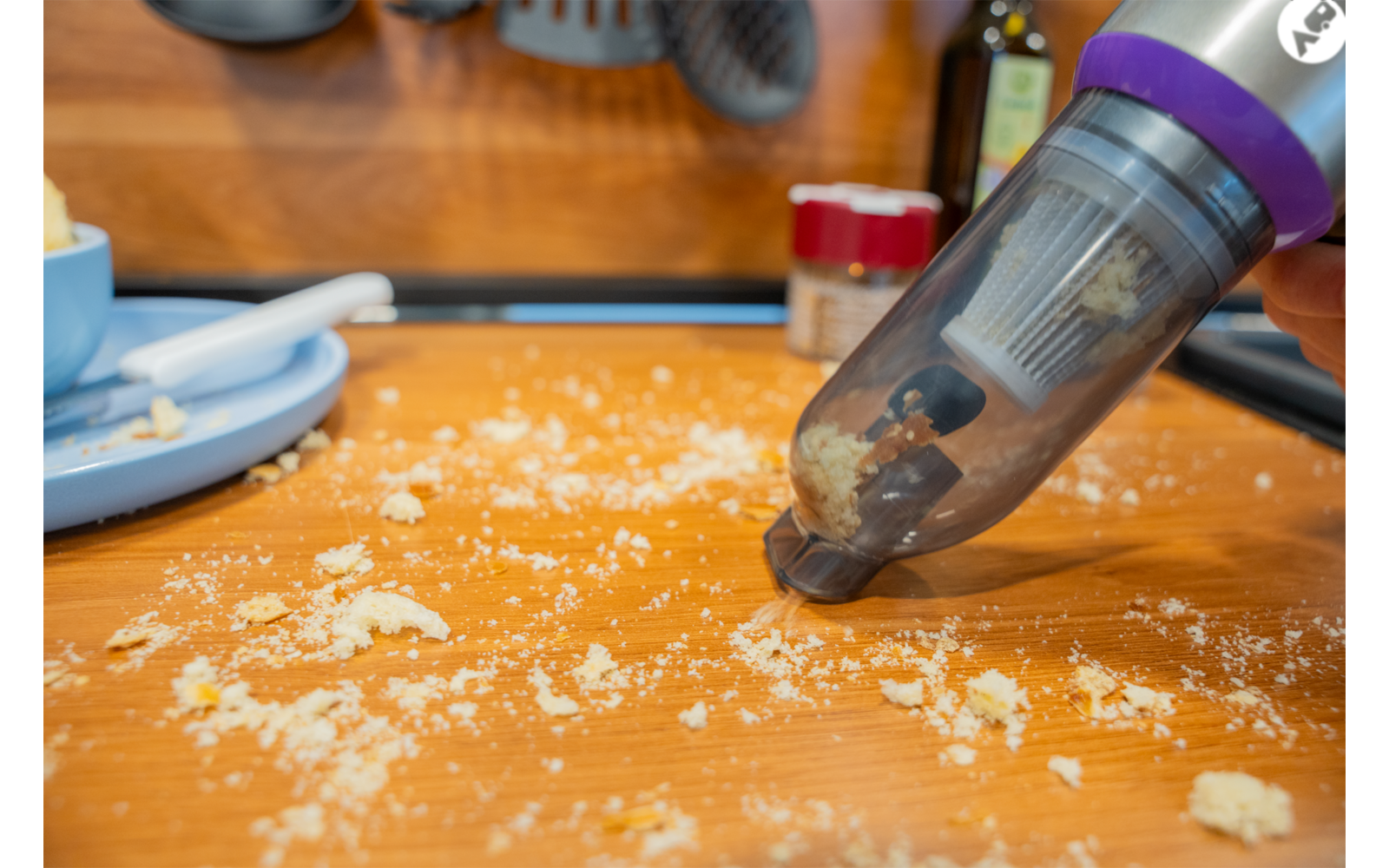 Main tenant un aspirateur à main sans fil au‑dessus de miettes éparpillées sur un plan de travail en bois