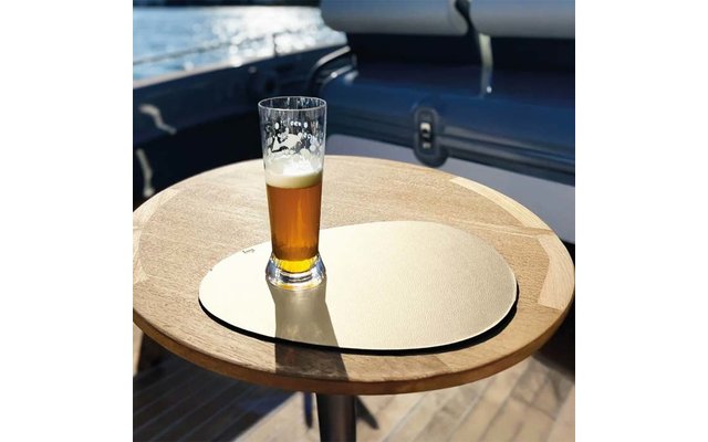 Halbvolles Pilsnerglas mit Schaum auf einer runden goldfarbenen Unterlage auf einem runden Holztisch; Bootsdeck und Wasser im Hintergrund