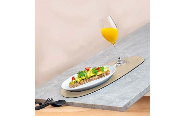 Scheibe Brot mit Samen, belegt mit Avocadoscheiben, halbierten Kirschtomaten und grünen Kräutern auf weißem Teller; Stielglas mit orangem Saft daneben; schwarze Gabel und Löffel auf grauem Tisch, beiger Hintergrund