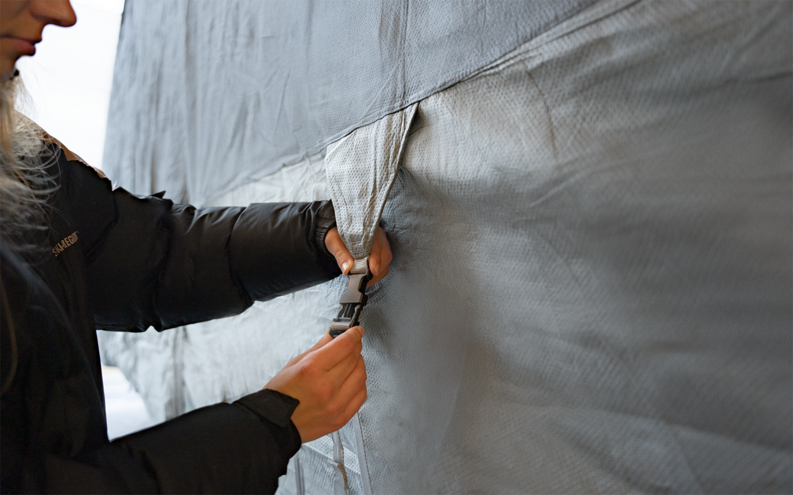 Hands of a person fastening a black buckle on a gray tarp