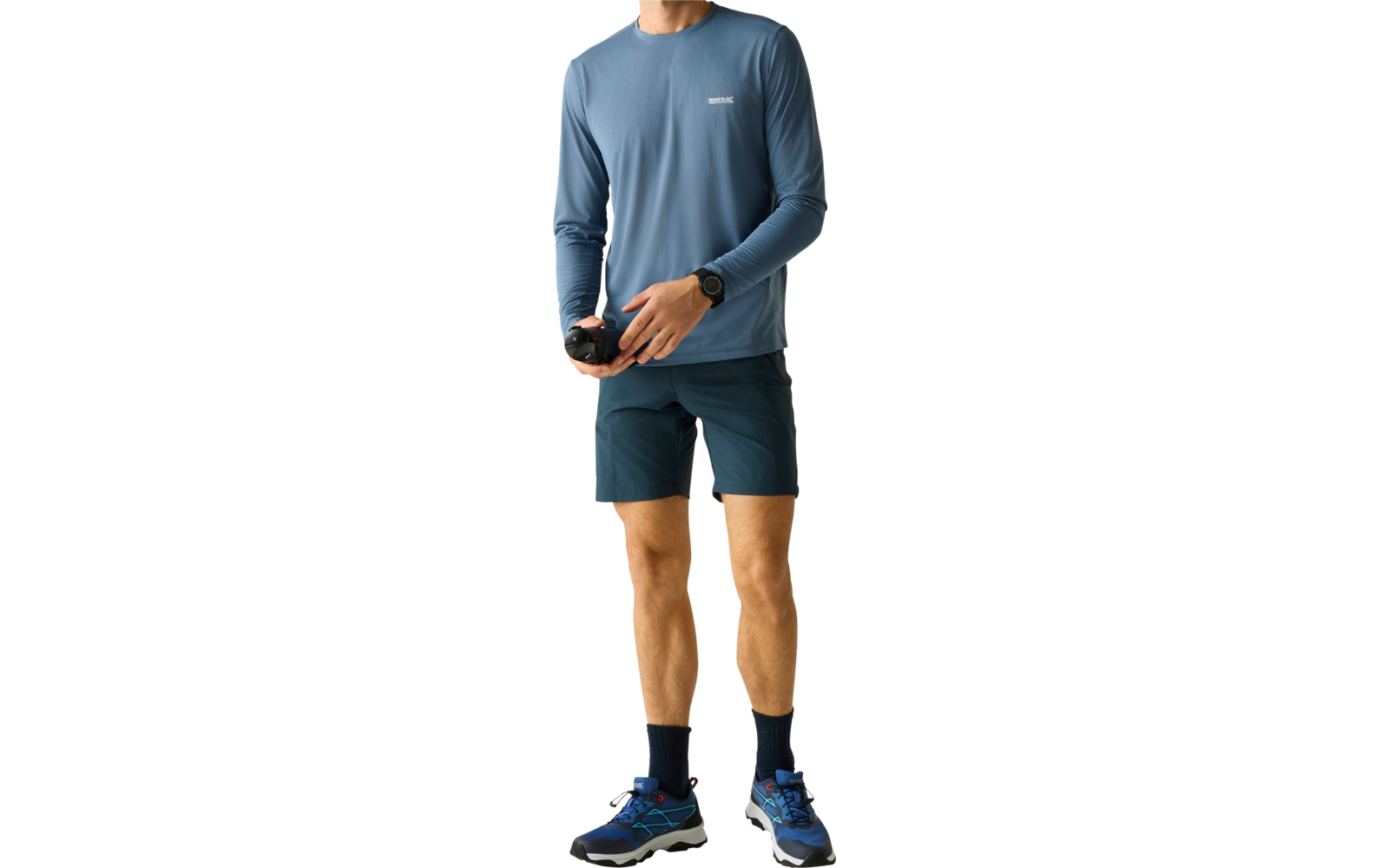 Oberkörper und Beine einer Person, Kopf nicht im Bild; blaues langärmeliges Shirt mit kleinem weißen Logo, dunkle Shorts, schwarze Socken, blaue Sportschuhe; Hände halten eine schwarze Kamera; schwarze Armbanduhr am linken Handgelenk