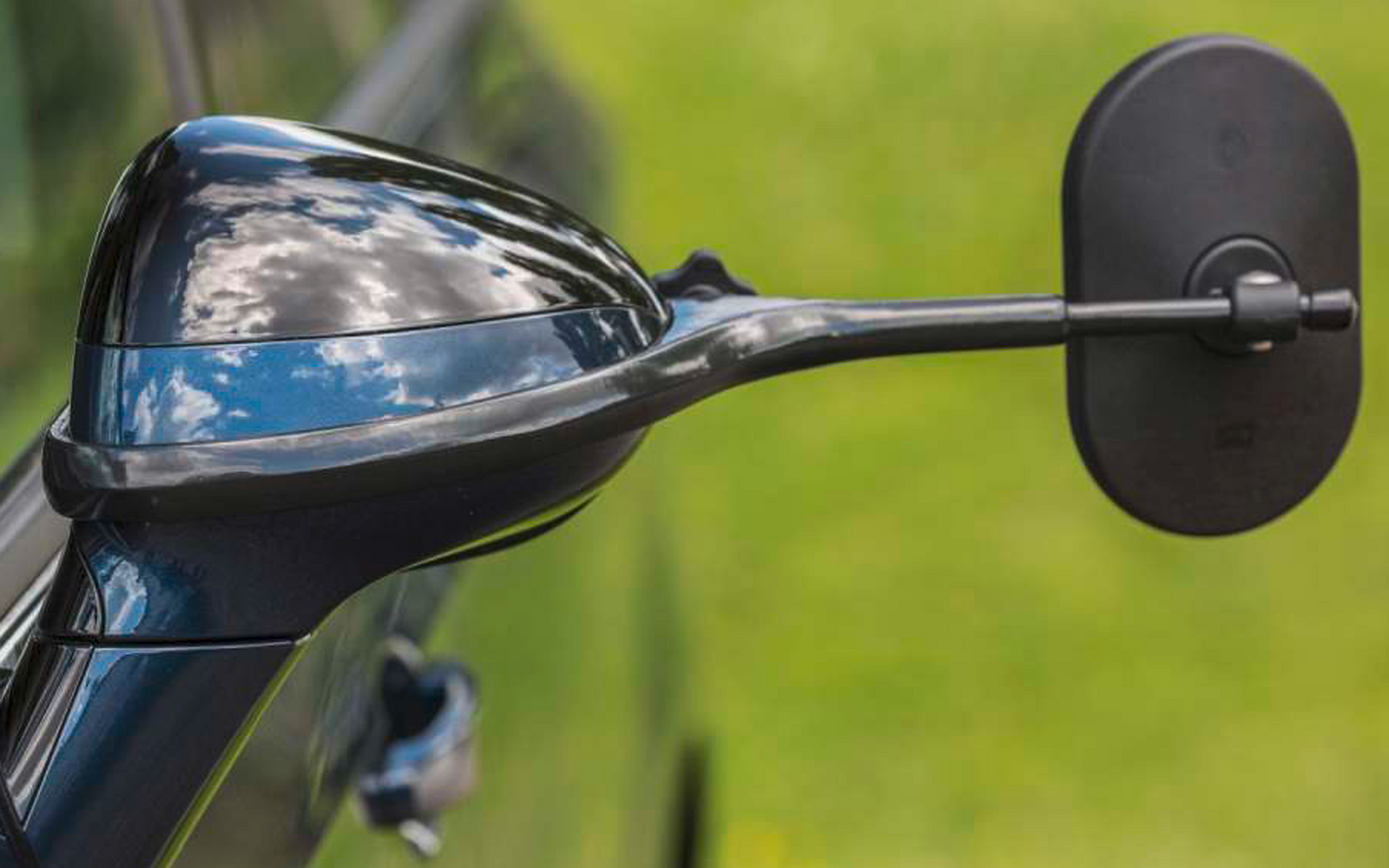 Nahaufnahme eines schwarzen Außenspiegels an einem Auto mit grüner Wiese im Hintergrund