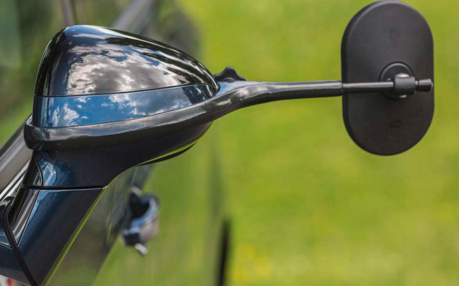 Nahaufnahme eines schwarzen Außenspiegels an einem Auto mit grüner Wiese im Hintergrund