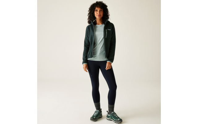 Frau mit lockigem Haar trägt Sportjacke, T-Shirt, Leggings und Sportschuhe, steht vor hellem Hintergrund