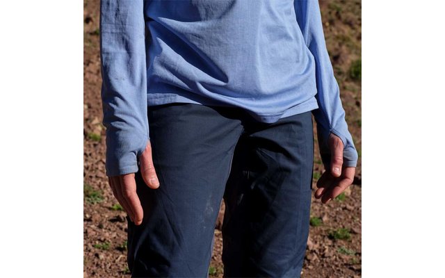 Oberkörper bis Oberschenkel einer Person in hellblauem Langarmshirt und dunkelblauen Hosen, Hände seitlich, trockener steiniger Boden im Hintergrund