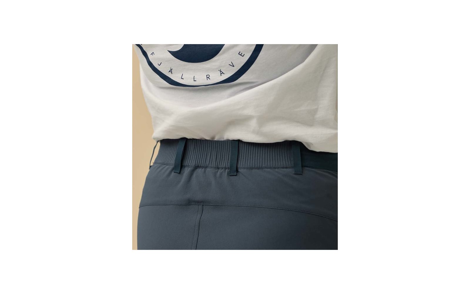 Unterer Rückenbereich mit weißem T‑Shirtsaum und rundem dunkelblauem Aufdruck, dunkelblaue Hose mit geripptem elastischem Bund und Gürtelschlaufen