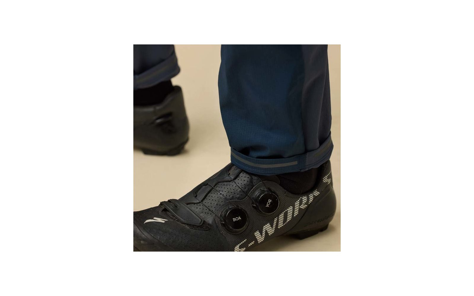 Nahaufnahme eines Fußes in schwarzem Fahrradschuh mit zwei runden Verschlüssen und dunkelblauer Hose