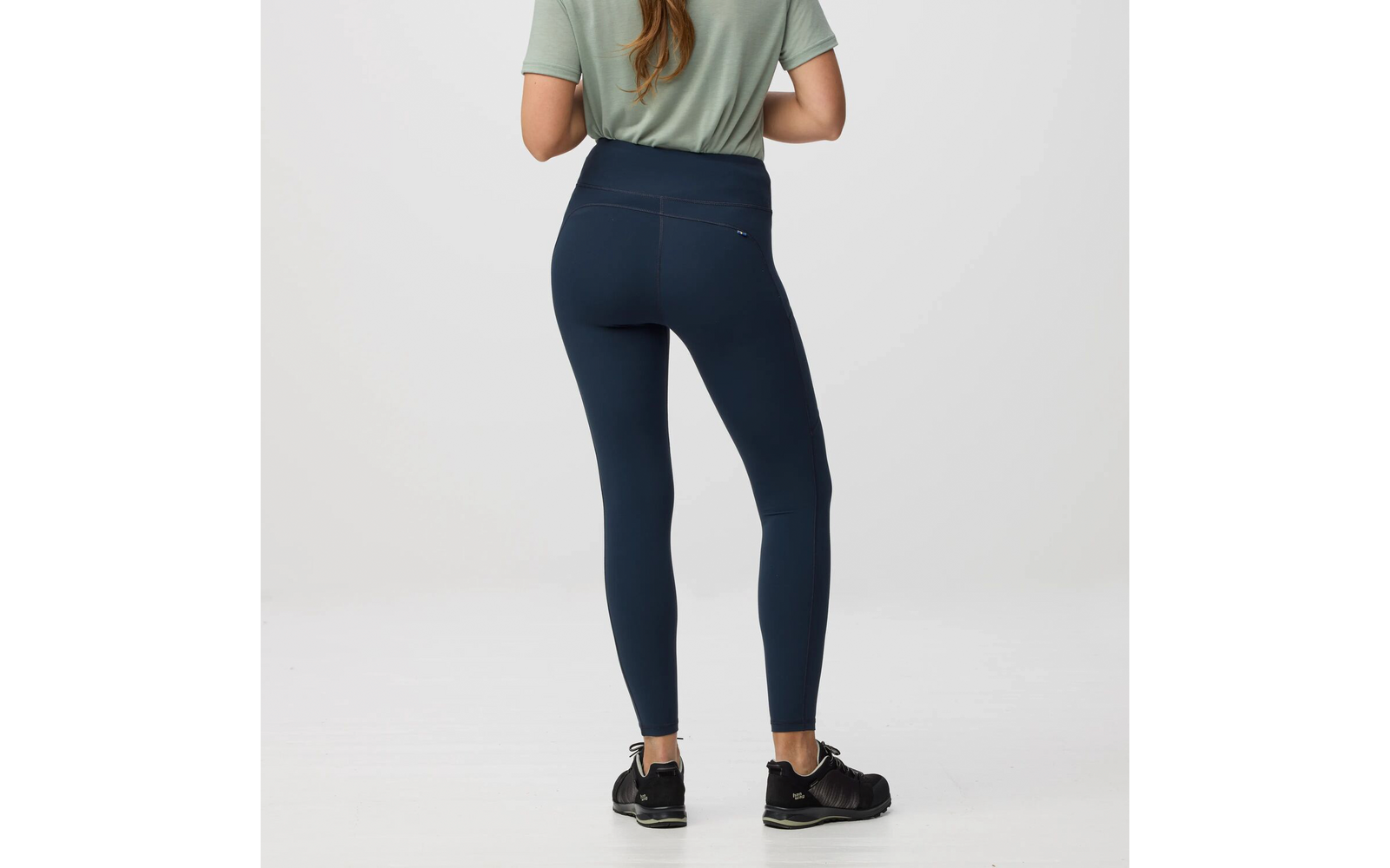 Vista trasera de una persona de pie con camiseta verde, mallas azul oscuro y zapatillas deportivas negras