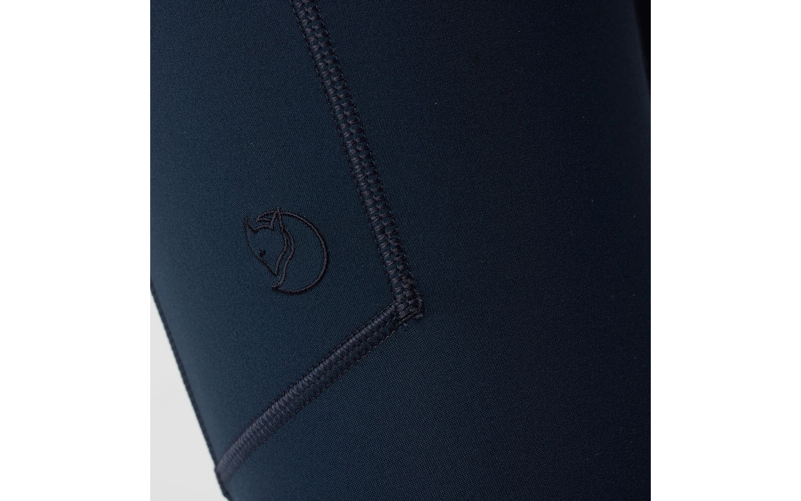 Plano detalle de tela azul oscuro con una costura visible y un logo de zorro bordado