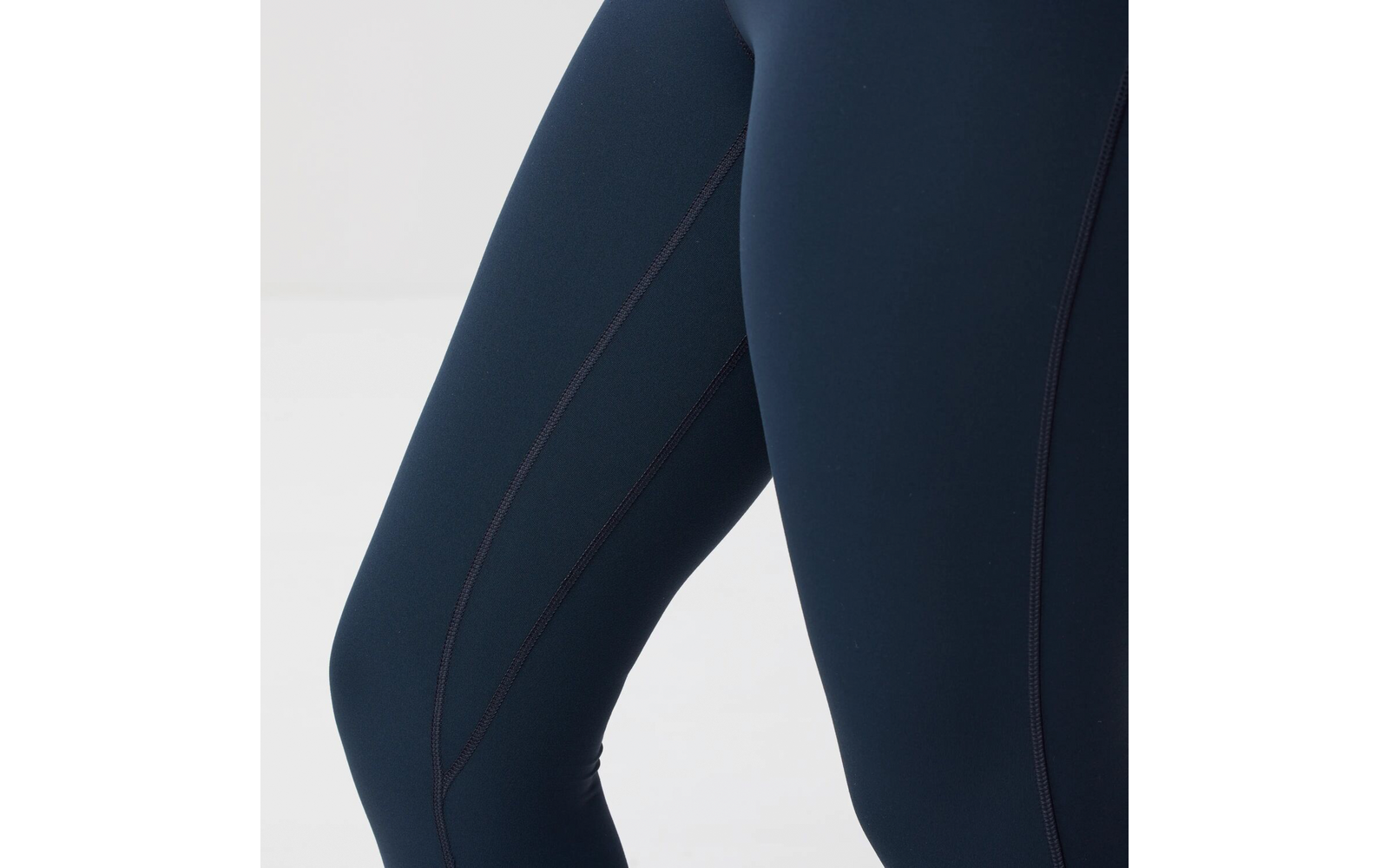 Primer plano de piernas con mallas deportivas azul marino oscuro con costuras visibles sobre fondo claro