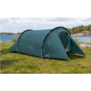 Green tunnel tent with open entrance on grass at a lakeshore; tent poles visible, rocks and trees on the opposite shore