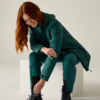 Person with long red hair sitting on a white cube, wearing a green coat and trousers, tying a shoelace