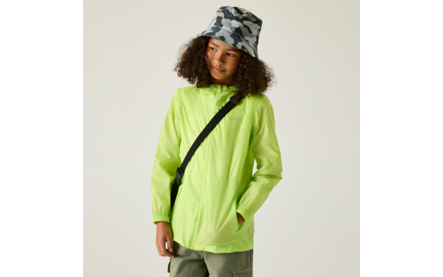 Kind mit lockigem dunklem Haar, neongrüne Regenjacke, Camouflage-Bucket-Hut, schwarze Umhängetasche quer über der Brust, Hände in den Taschen, Blick nach rechts, heller Hintergrund