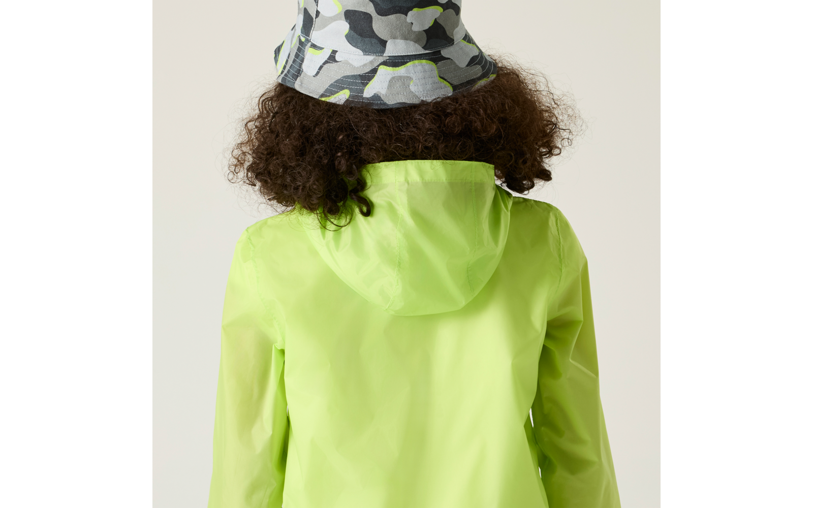 Person von hinten, lockige braune Haare, leuchtend grüner Regenmantel mit Kapuze, grauer Camouflage-Fischerhut mit hellgrünen Akzenten