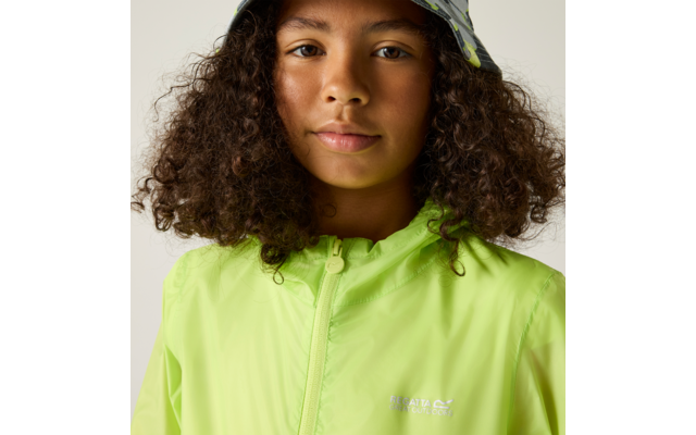 Nahaufnahme einer Person mit lockigen Haaren, einer neongrünen Regenjacke mit Reißverschluss und einem gemusterten Fischerhut vor hellem Hintergrund