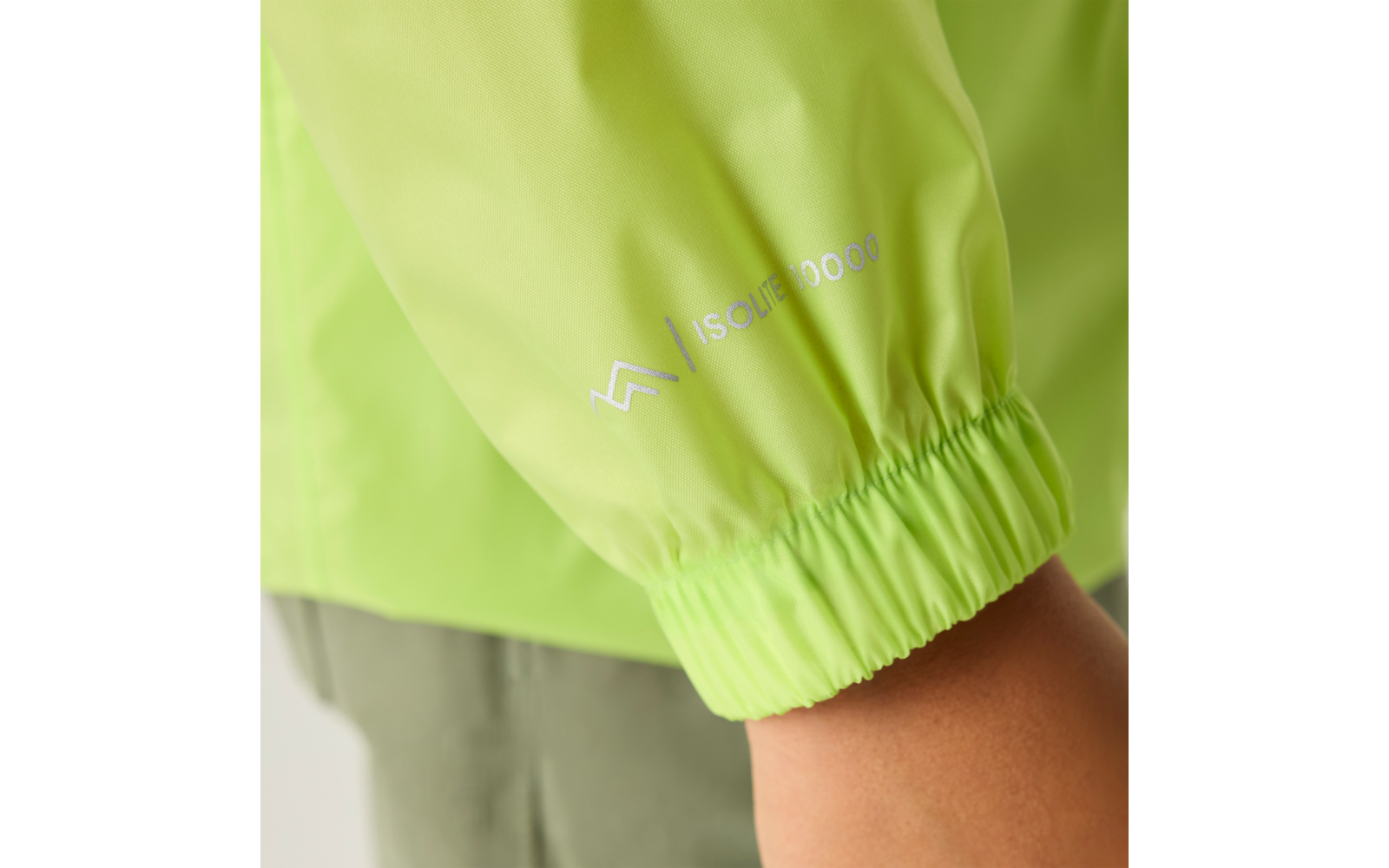 Nahaufnahme eines limettengrünen Jackenärmels mit elastischer Manschette, weißem Logo und weißem Textdruck, sichtbarer Unterarm und graue Hose im Hintergrund