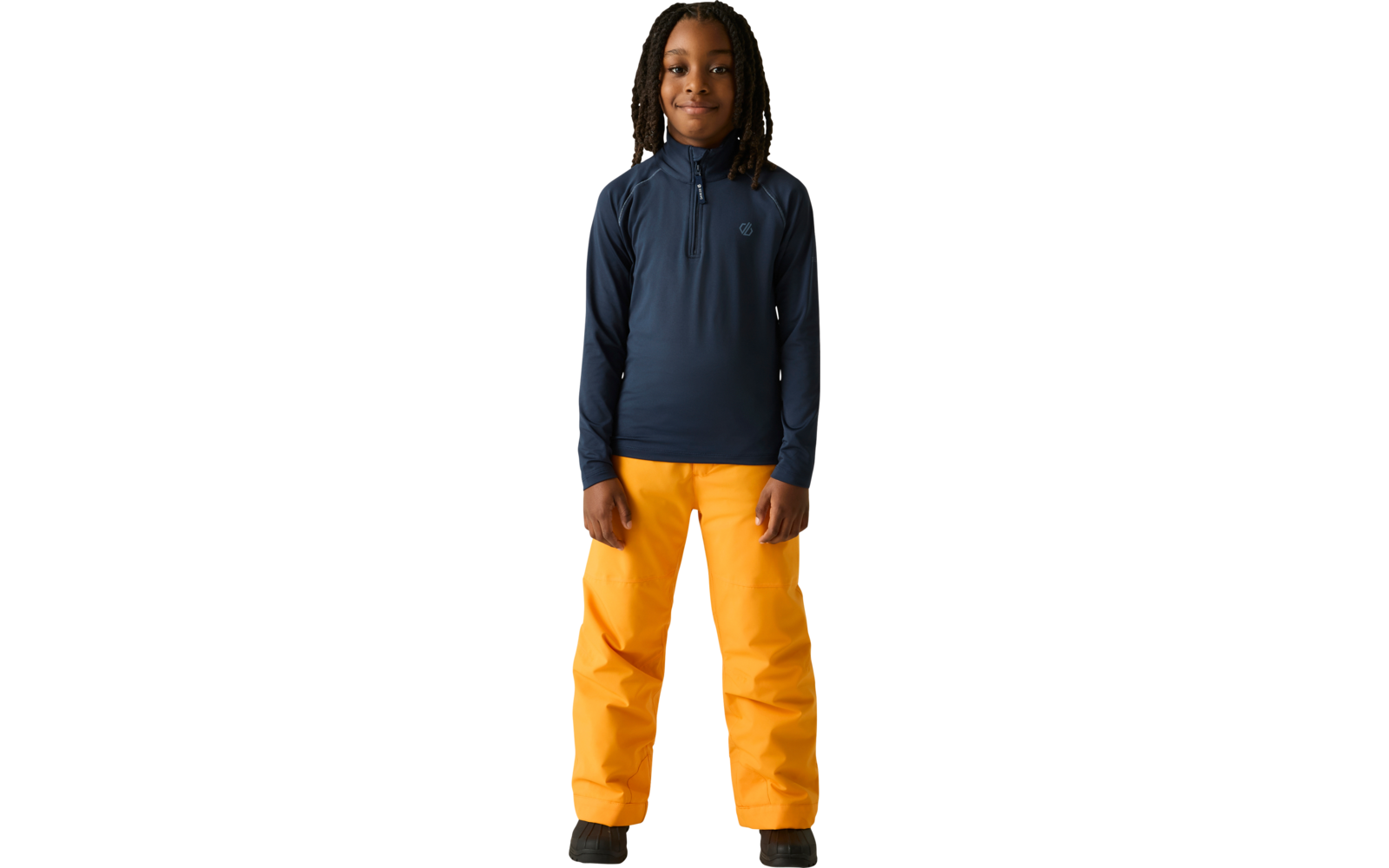 Persoon staat recht voor een lichte achtergrond, draagt een donkerblauw shirt met rits en lange mouwen, feloranje broek, zwarte schoenen, haar in vlechten