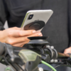 Hand hält Smartphone mit rundem schwarzem Griff über einer Halterung am Fahrradlenker