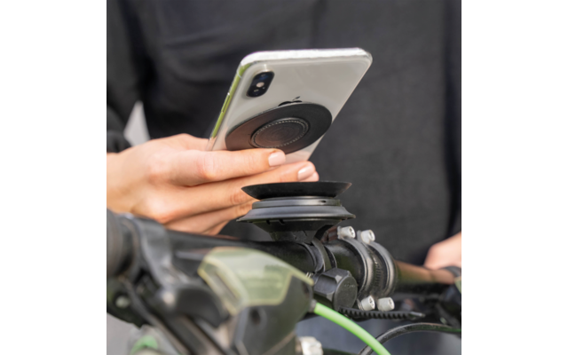Hand hält Smartphone mit rundem schwarzem Griff über einer Halterung am Fahrradlenker
