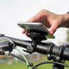 Hand hält Smartphone in einer am Fahrradlenker montierten Halterung; grüne Bremsleitung sichtbar