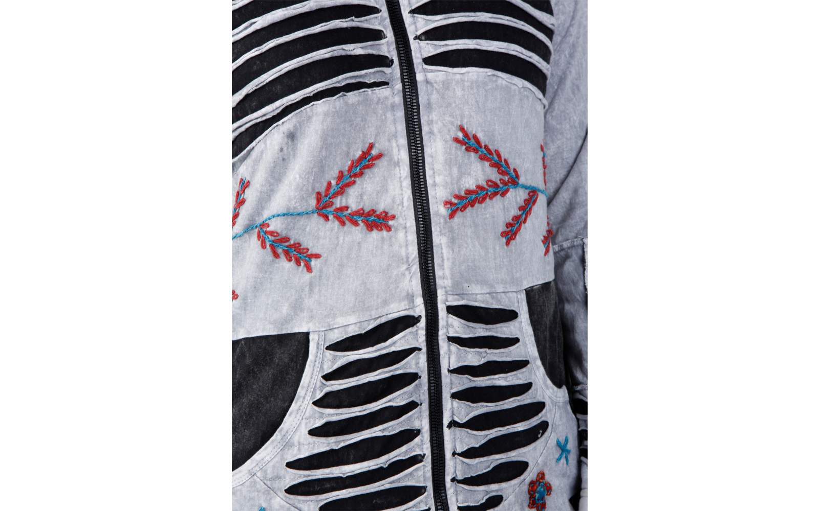 Nahaufnahme einer hellgrauen Jacke mit schwarzem Reißverschluss, horizontalen Schlitzen mit schwarzem Unterstoff, roten und blauen, zweigartigen Stickereien und sichtbarer Vordertasche