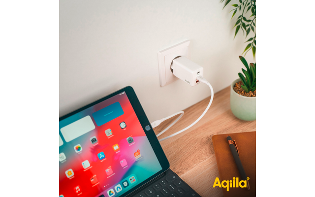 Tablet mit farbigem Bildschirm, das per Kabel an eine Wandsteckdose angeschlossen ist, neben einem Blumentopf