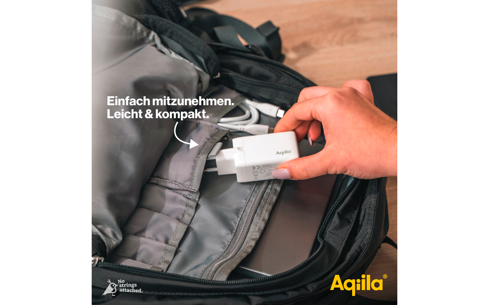 Hand packt Kleidung in einen offenen grauen Rucksack auf einem Holzboden