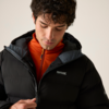Person mit dunklem, gewelltem Haar blickt nach unten und zieht den Reißverschluss einer schwarzen Steppjacke hoch; darunter eine orangefarbene Jacke