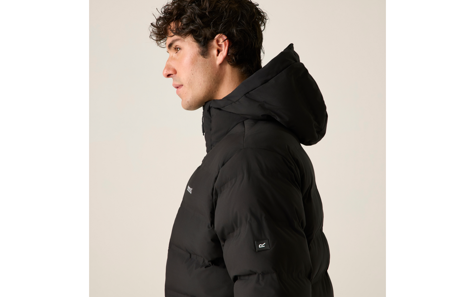 Person im Profil trägt eine schwarze Daunenjacke mit Kapuze, Blick nach links, heller Hintergrund