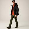 Person in schwarzer Steppjacke, orangefarbenem Pullover, olivgrünen Hosen, schwarzen Schuhen und schwarzer Schirmmütze vor hellem Hintergrund, gehend