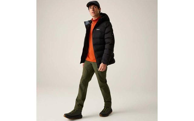 Person in schwarzer Steppjacke, orangefarbenem Pullover, olivgrünen Hosen, schwarzen Schuhen und schwarzer Schirmmütze vor hellem Hintergrund, gehend