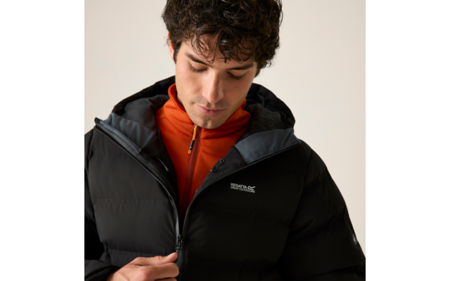 Person mit dunklem, gewelltem Haar blickt nach unten und zieht den Reißverschluss einer schwarzen Steppjacke hoch; darunter eine orangefarbene Jacke