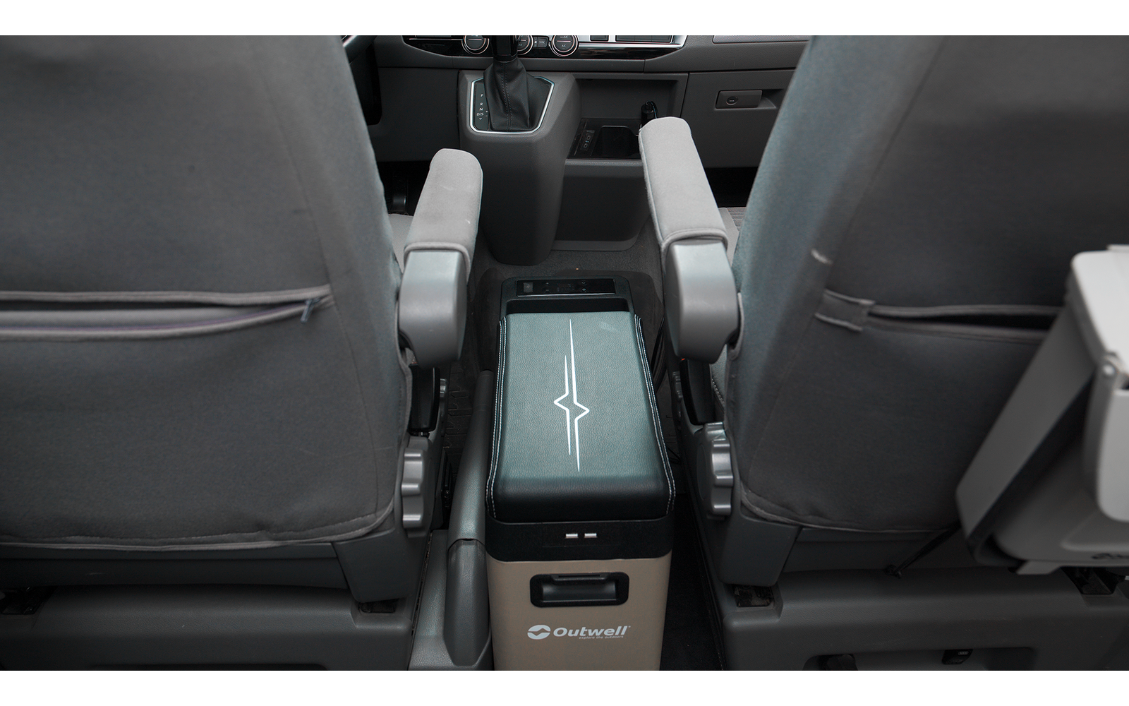 Blick zwischen zwei grauen Vordersitzen auf eine mittige Konsole mit rechteckigem gepolstertem Aufsatz und heruntergeklappten Armlehnen; auf dem Aufsatz ein weißes Sternsymbol