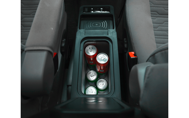 Mittelkonsole eines Autos zwischen den Vordersitzen mit vier Getränkedosen in den Haltern: zwei rote Dosen und zwei silberne Dosen mit grünen Oberseiten; sichtbare Sitzbezüge und rote Gurtverschlüsse