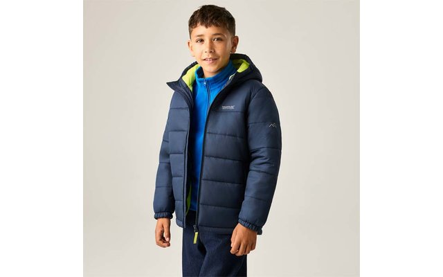 Person mit kurzen dunklen Haaren, trägt eine marineblaue gesteppte Jacke mit grün gefütterter Kapuze und einen blauen Reißverschluss-Pullover, steht vor hellem Hintergrund
