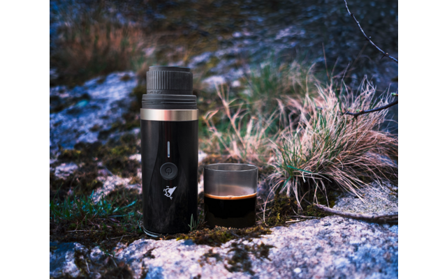 Thermoskanne und Tasse stehen im Gras neben einem schneebedeckten Weg