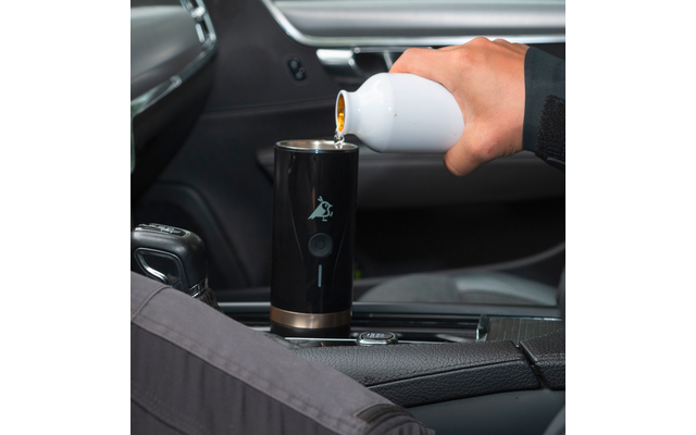 Hand hält einen Autoschlüssel über einem schwarzen Becherhalter in einem Fahrzeug