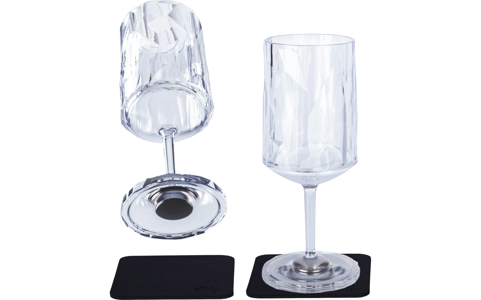Two clear wine glasses with faceted design, one standing and one lying on its side, each on a black coaster