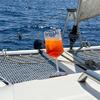 Wine glass with orange-red drink on the deck of a sailboat, trampoline netting, ropes, rigging and open sea in the background