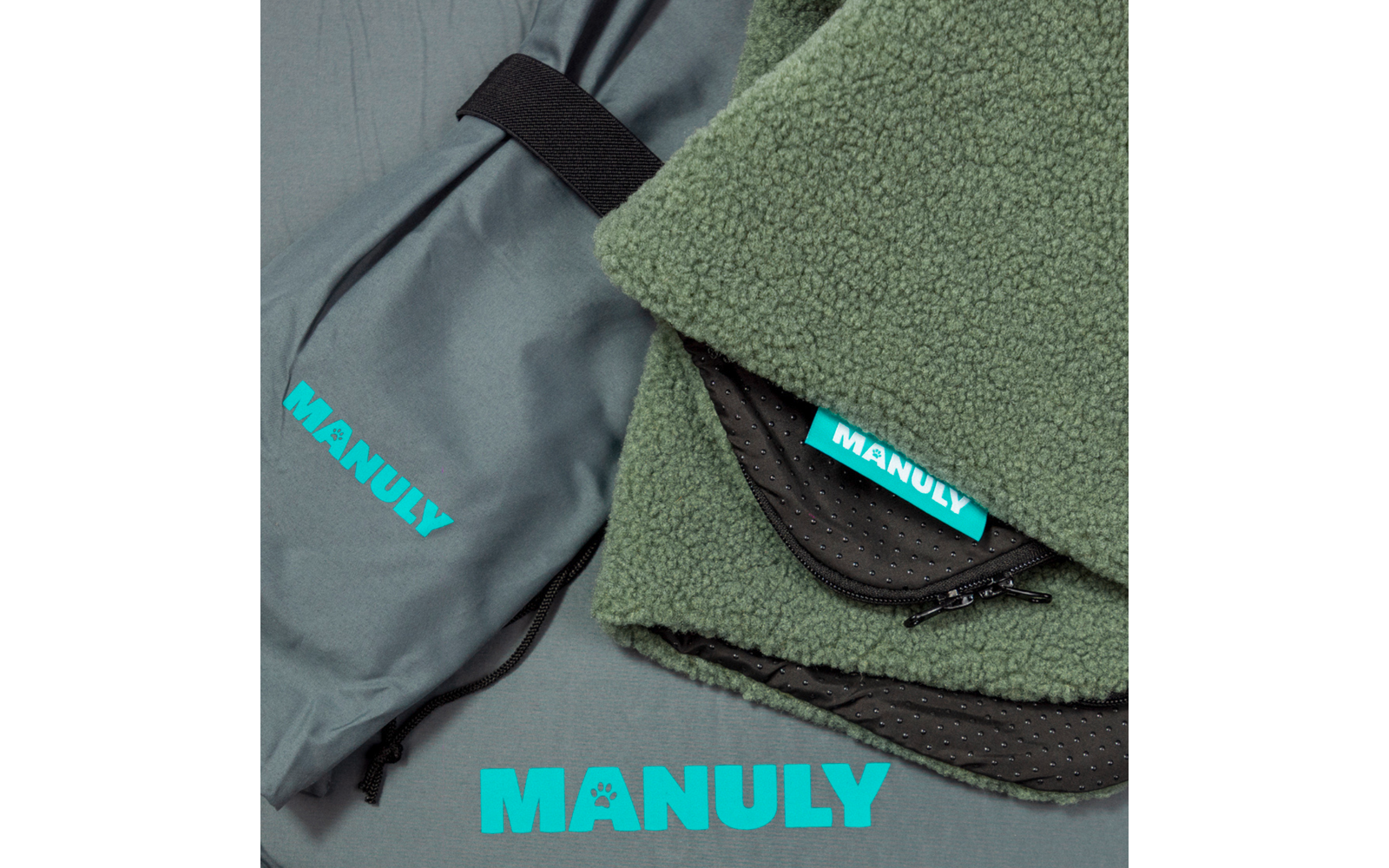 Gefaltetes grünes Fleece mit Reißverschluss und türkisfarbenem Etikett 'MANULY'; graue Tasche mit schwarzem Band und türkisfarbenem Schriftzug 'MANULY'