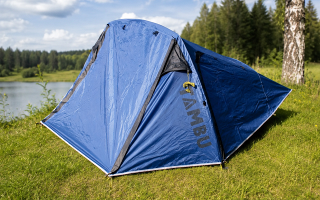 Tente bleue sur l'herbe au bord d'un lac, arbres et ciel nuageux en arrière-plan