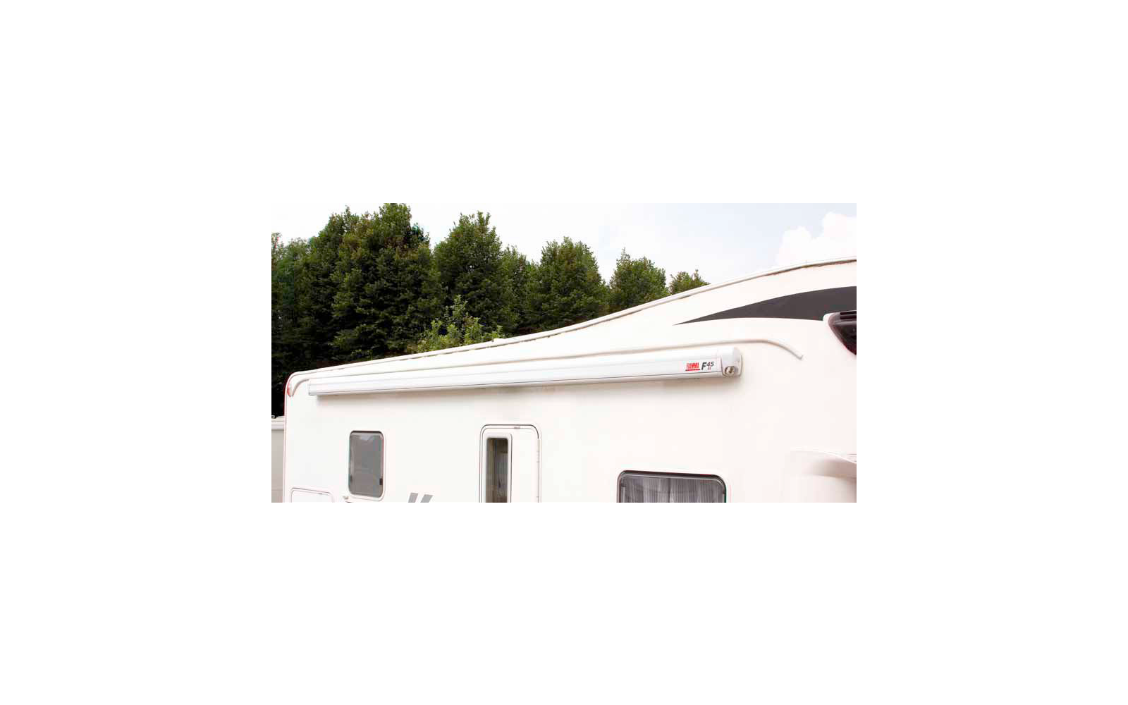 Gedeeltelijk zicht op een witte camper met uitgeschoven luifel, bomen op de achtergrond
