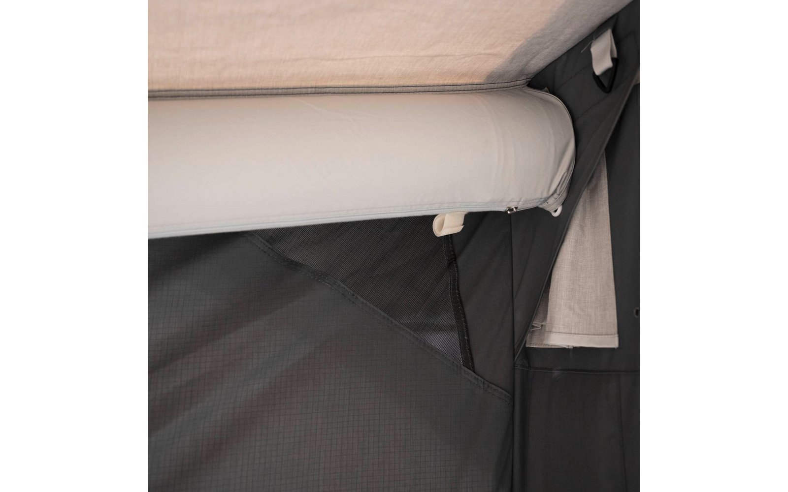 Beige gerolltes Polster an hellgrauer Oberkante über dunklem grauem Stoff, mit sichtbarer Naht, Reißverschluss und kleinem weißen Kunststoffhaken