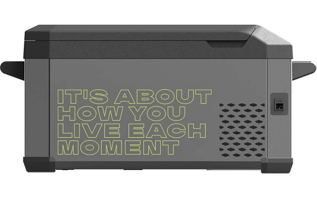 Graues rechteckiges Gerät mit Deckel, seitlichen Griffen, Lüftungsgitter und Steckdose; große gelbgrüne Schrift auf der Seite: IT'S ABOUT HOW YOU LIVE EACH MOMENT