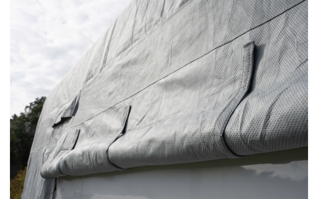 Gray, folded, textured fabric draped over a white smooth edge; trees on the left, cloudy sky above